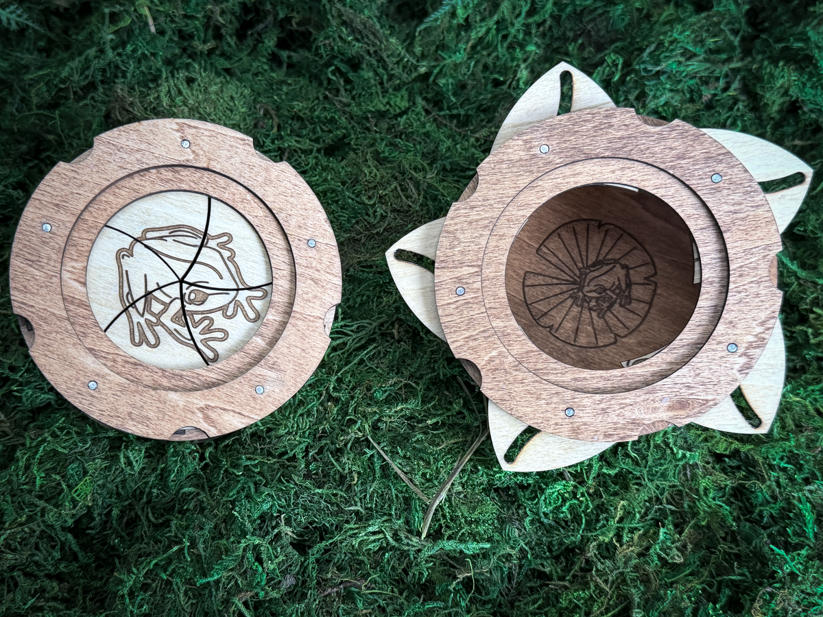 Top view of a wooden frog iris box shown open and closed, revealing a hidden frog on a lily pad engraving inside the storage compartment.