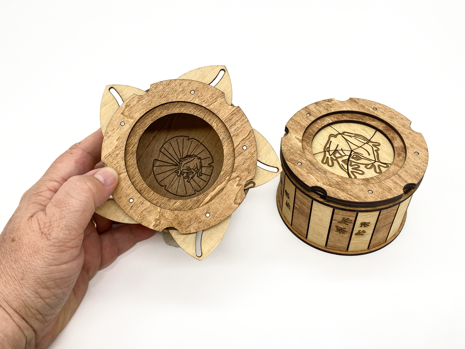 Frog Keepsake Box shown in hand to demonstrate size with the twist-open iris lid revealing the engraved frog on a lily pad inside.