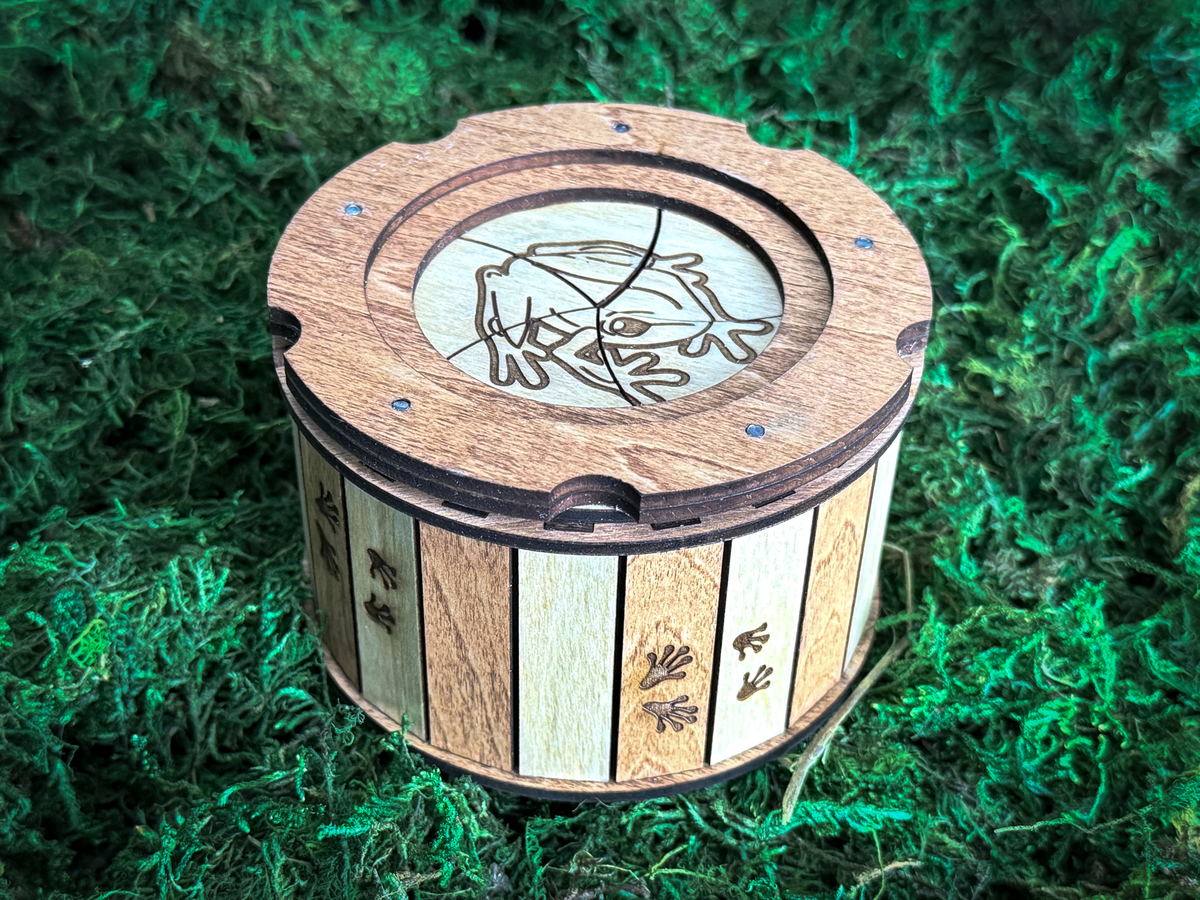 Close-up of a wooden frog iris keepsake box with an engraved frog on the lid, alternating natural and stained wood panels, and tiny frog footprints.