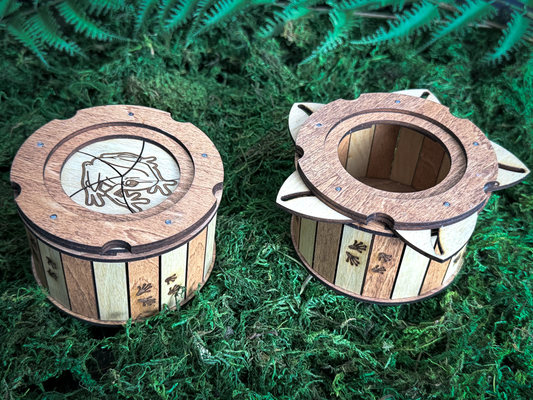 Frog wooden iris box shown closed and open on green moss, displaying the engraved frog lid, rotating wooden petals, and storage compartment.