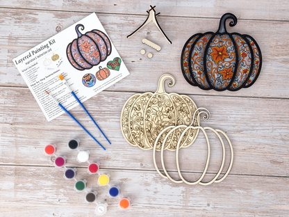Unpainted Gothic Pumpkin layered wood artwork displayed with paint pots, brushes, stand pieces, candle, and greenery on a rustic background.