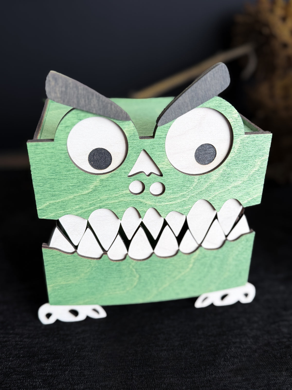 Front view of a green wooden monster trinket box with its hinged mouth closed, showing interlocking white teeth and expressive googly eyes.