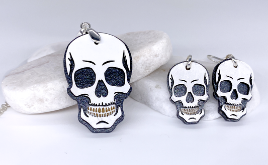 Layered wood skull necklace and matching earrings displayed on white stones.