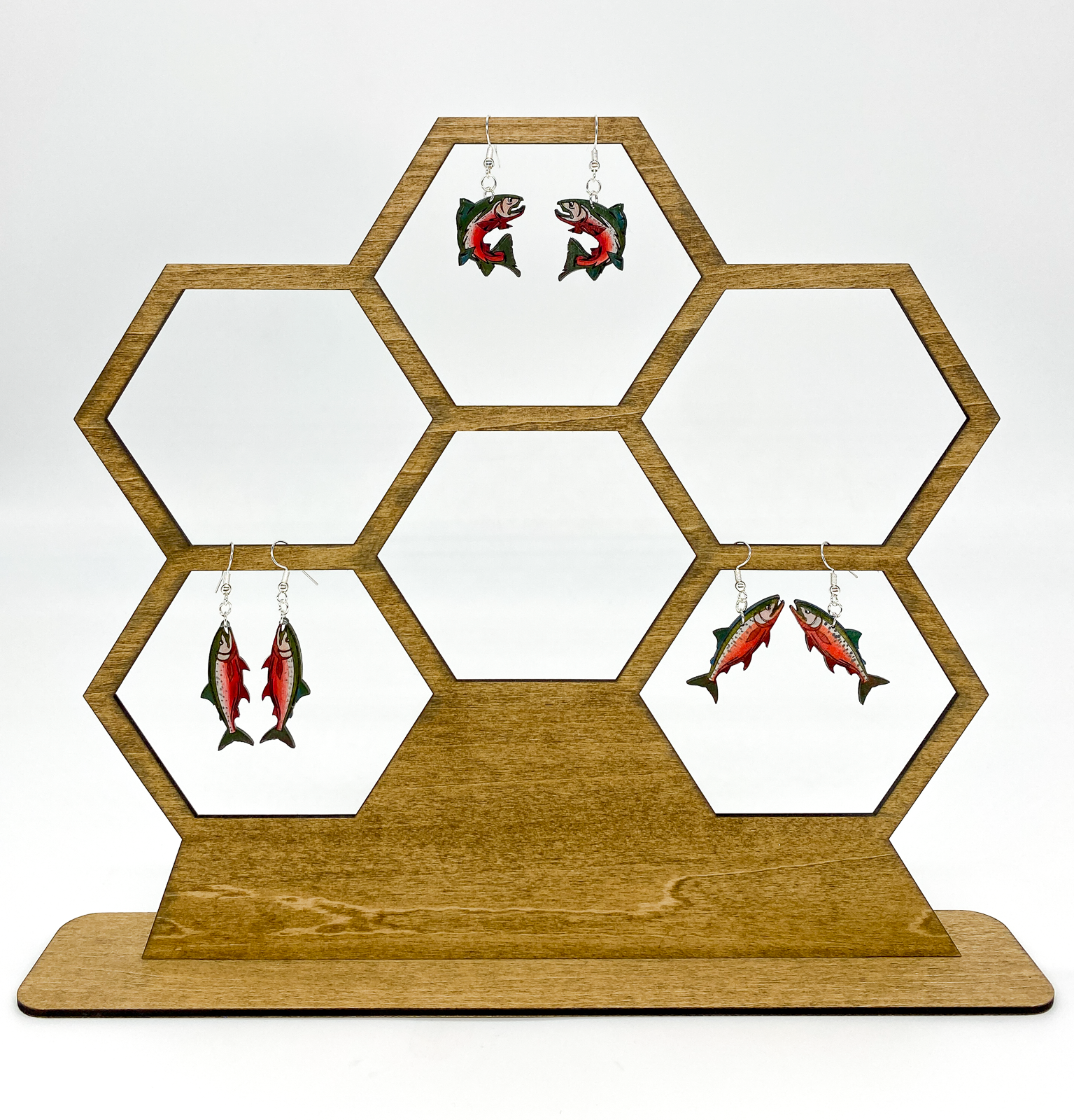 Hexagonal wooden earring display with fish-themed earrings on a white background
