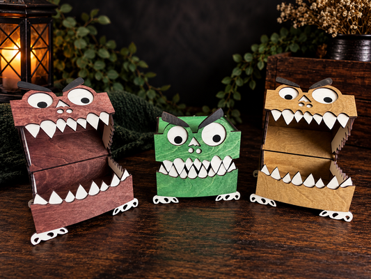 Three hand-stained wooden monster trinket boxes arranged together with googly eyes, toothy grins, and small white feet on a dark tabletop.