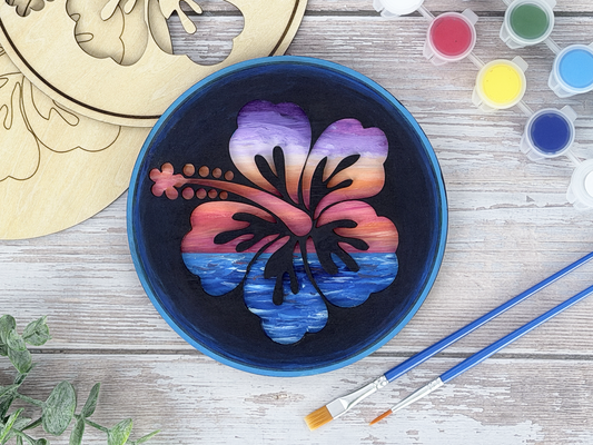 Finished hawaiian hibiscus adult craft kit shown with painted layered wood artwork, unpainted kit pieces, paint pots, and brushes on a rustic wood background.