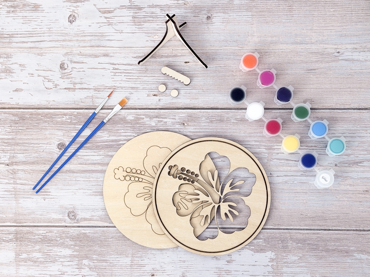 Unpainted Hawaiian Hibiscus layered wood painting kit pieces with paint pots, brushes, stand, and display hardware on a rustic background.