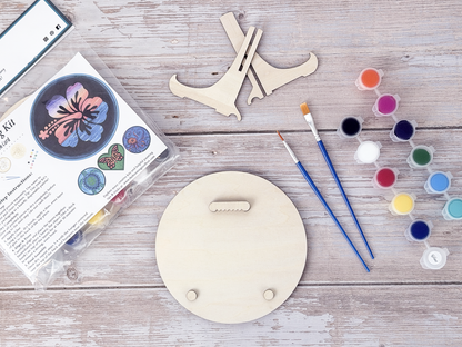 Back view of the Hawaiian Hibiscus wood craft kit showing hanger piece, bumpers, paint pots, brushes, packaging, and stand.