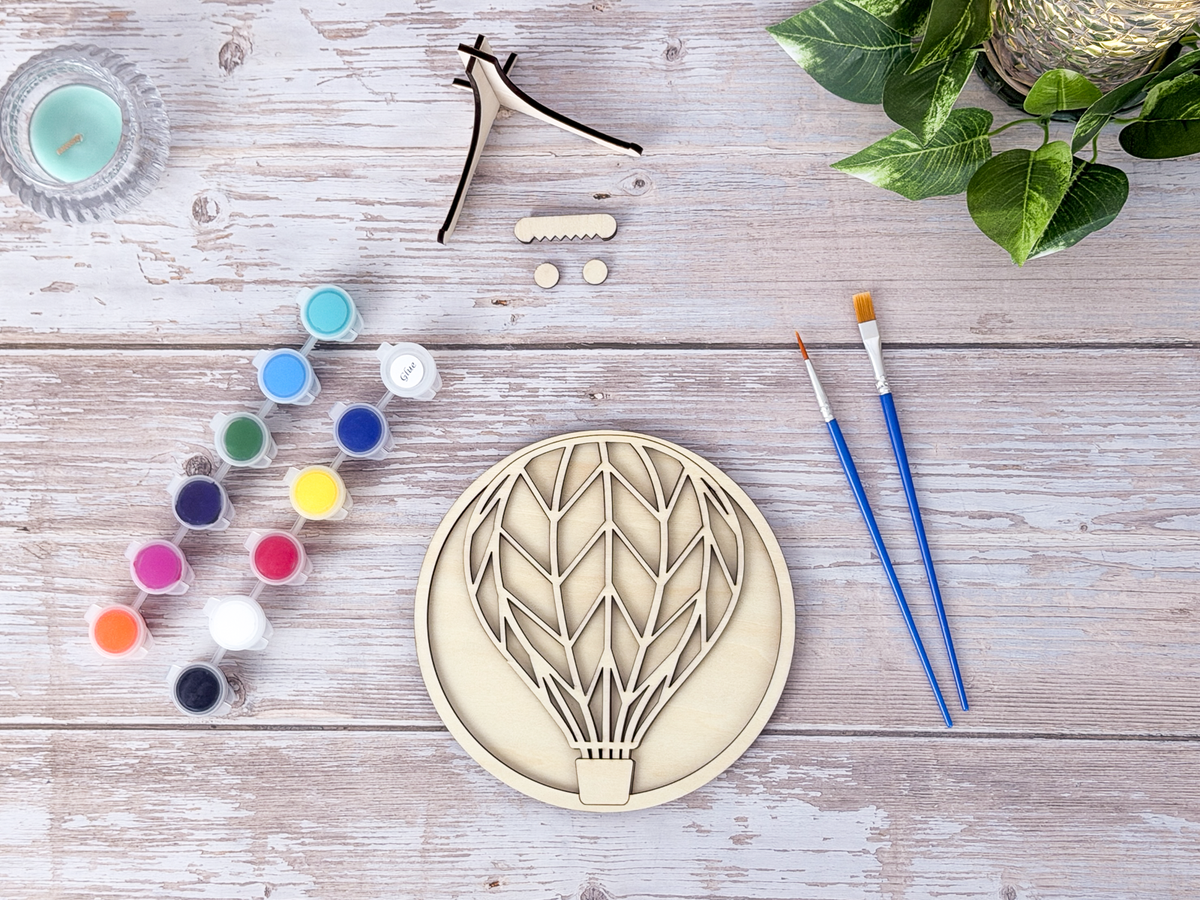 Unpainted Hot Air Balloon DIY wood craft kit centered with acrylic paint pots, brushes, display stand, and hardware.