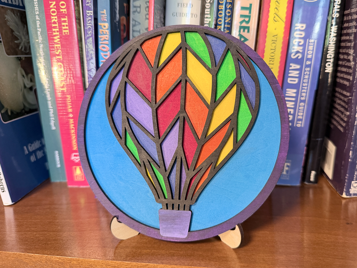 Finished Hot Air Balloon layered wood artwork painted in bright rainbow colors and displayed on a small wooden stand.