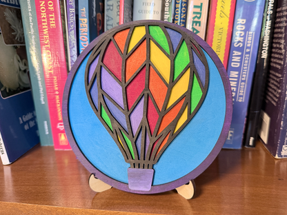 Finished Hot Air Balloon layered wood artwork painted in bright rainbow colors and displayed on a small wooden stand.