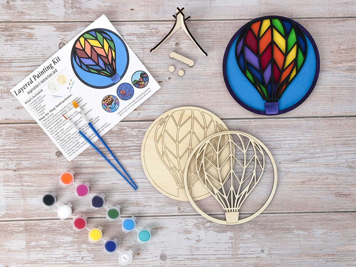 Hot Air Balloon wood painting kit with unfinished layered pieces, finished painted example, paint pots, brushes, and instruction card.