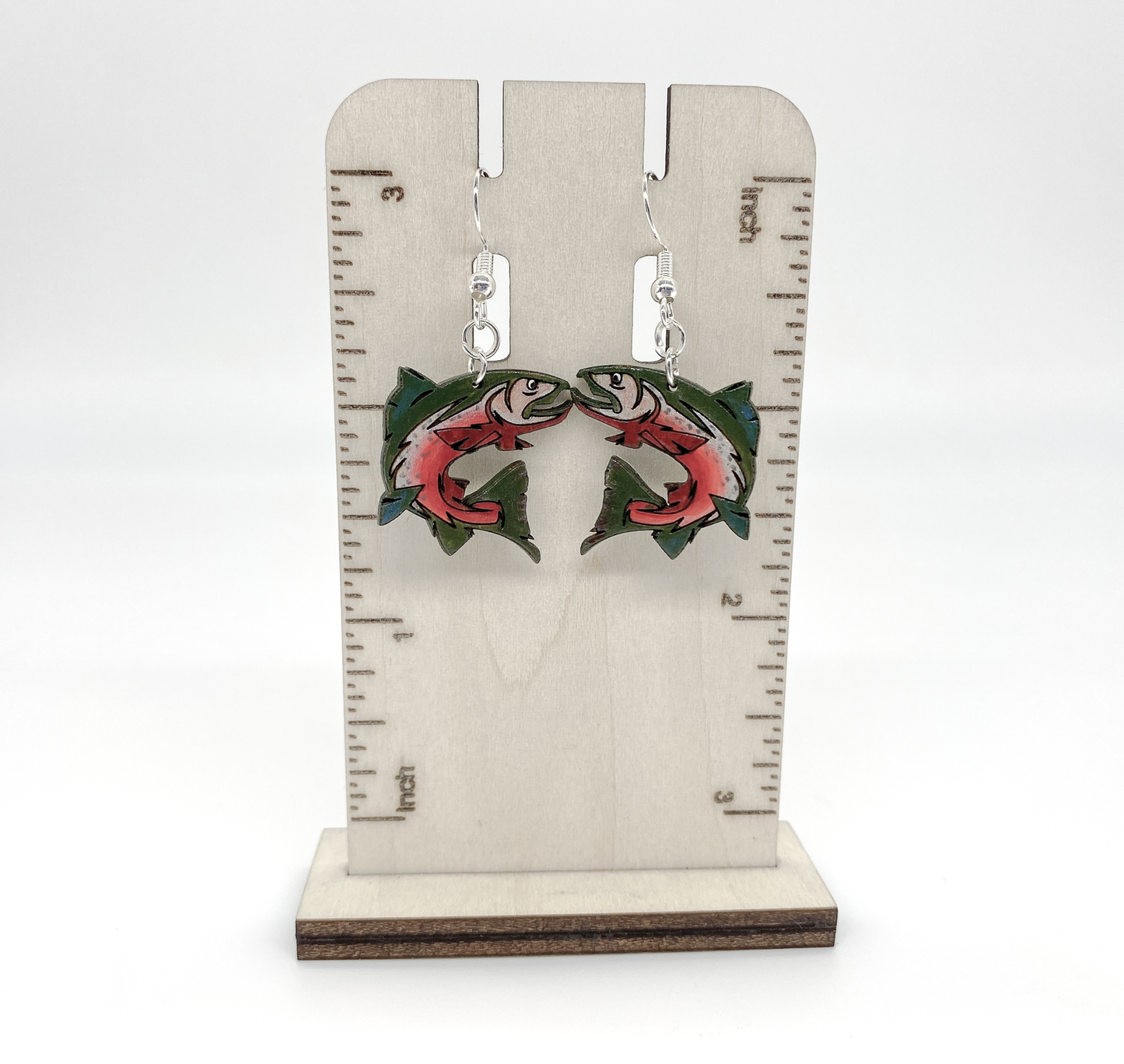 Earrings with fish design on a wooden stand with measurement scale