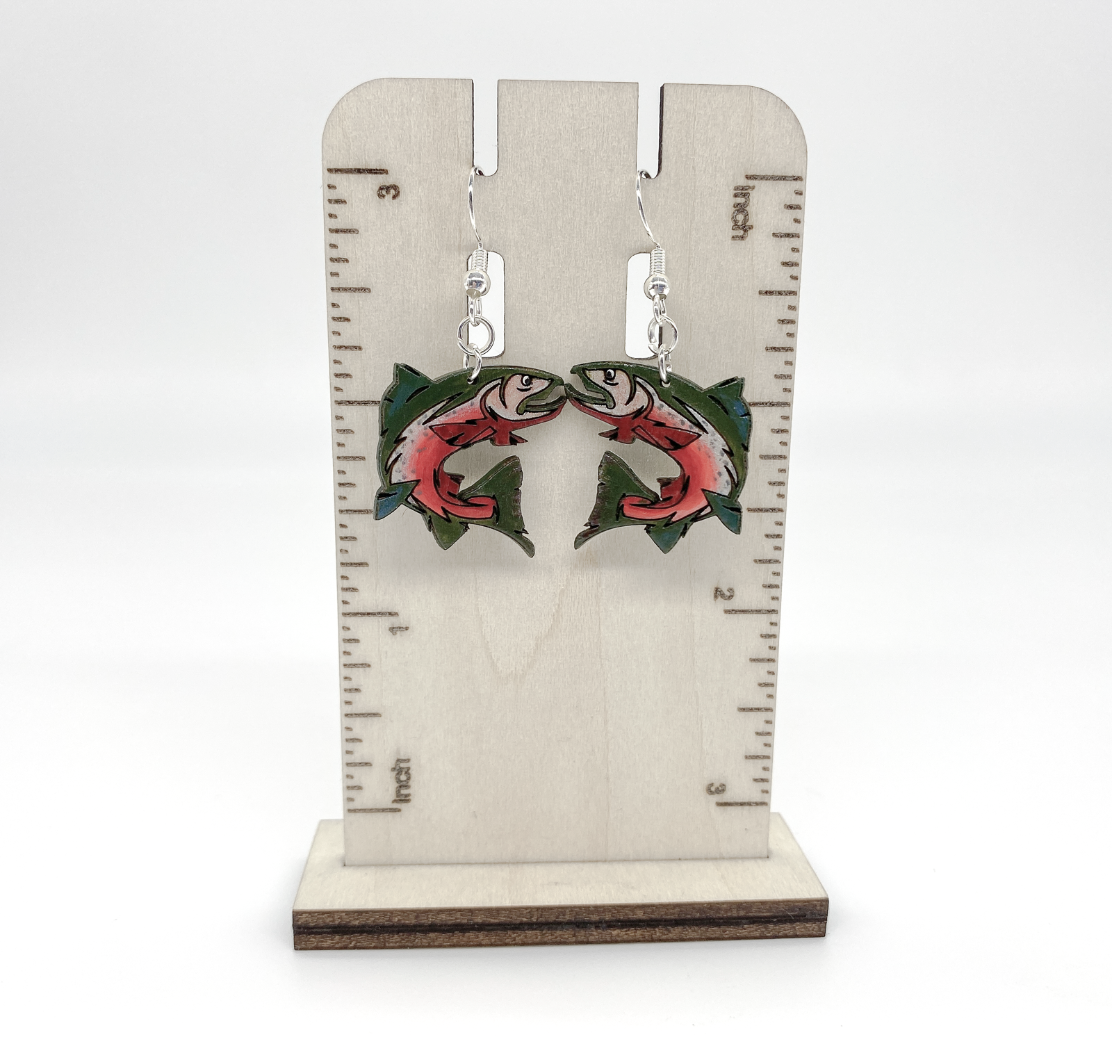 Earrings with fish design on a wooden stand with measurement scale