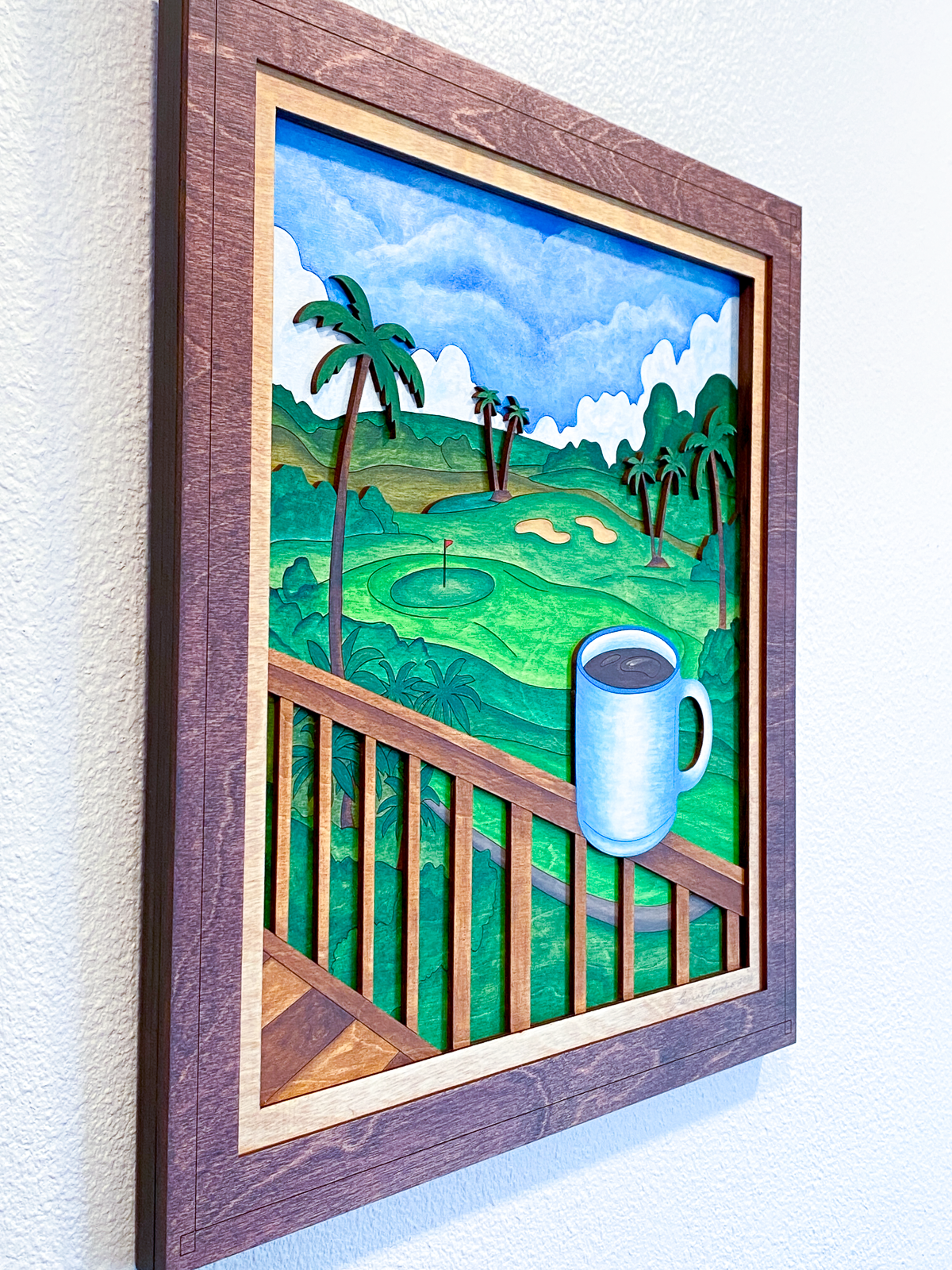 Close angled detail of Lanai Mornings layered sculptural wall art emphasizing the depth of the laser-cut wood layers, hand-painted tropical landscape, and dimensional coffee cup foreground.