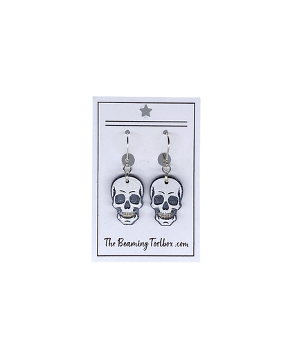 Hand-painted layered wood skull earrings on branded display card with silver-plated leverback hooks.