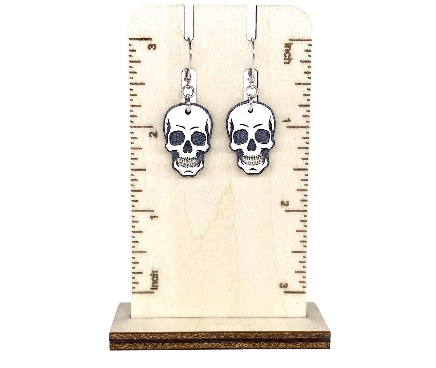 Layered wood skull earrings shown on a wooden ruler display for size reference.
