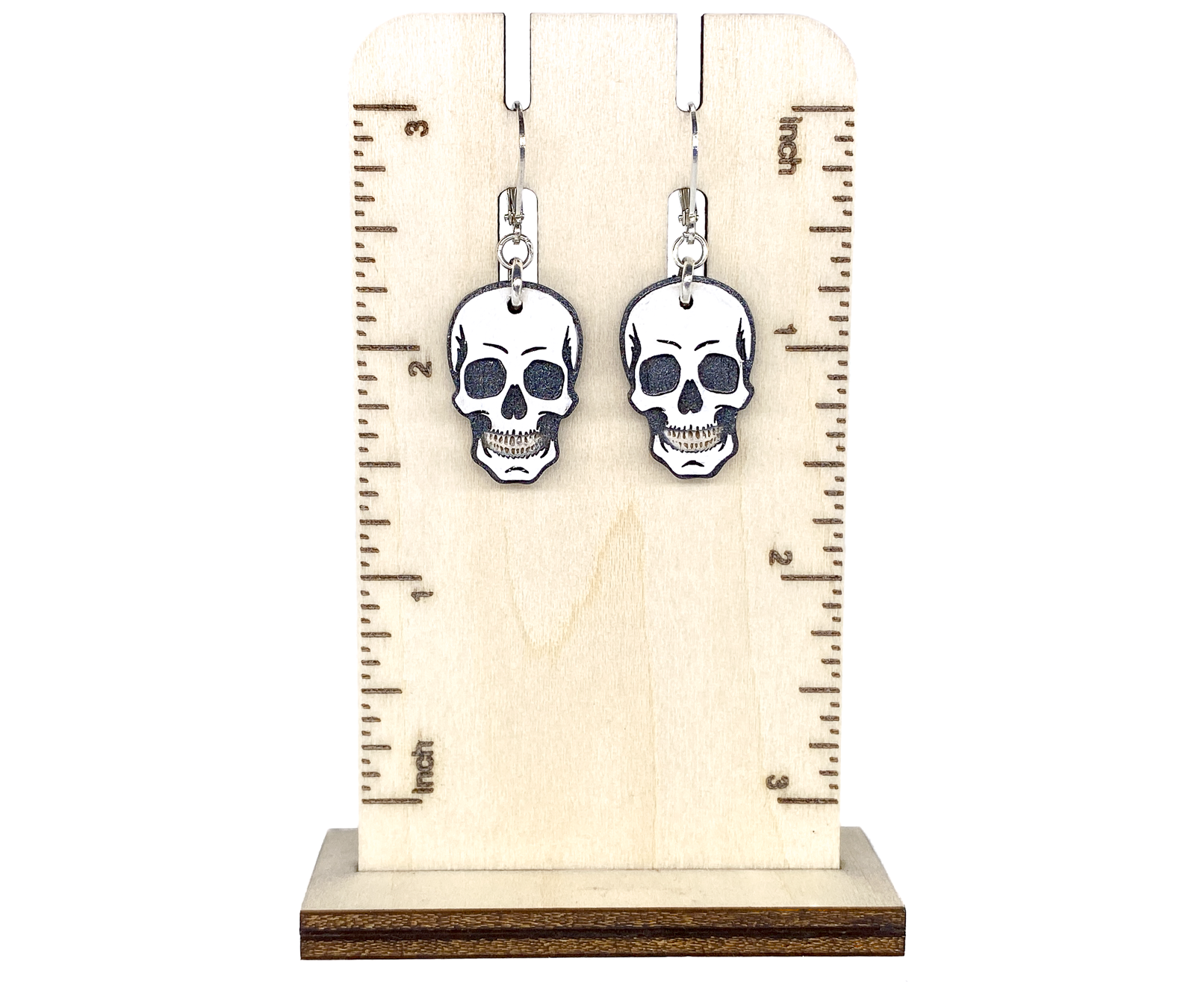 Layered wood skull earrings shown on a wooden ruler display for size reference.
