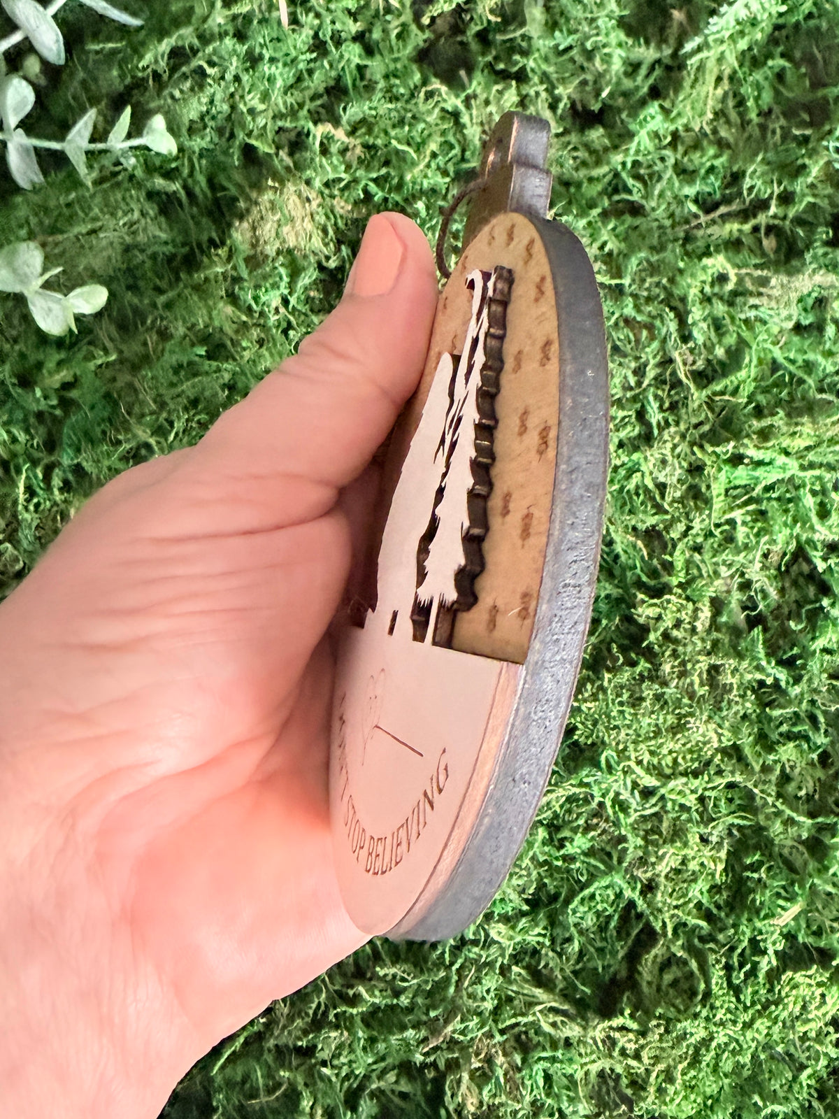 Side view of a handcrafted wooden Sasquatch Christmas ornament showing the layered construction, raised design, and dark finished edges.