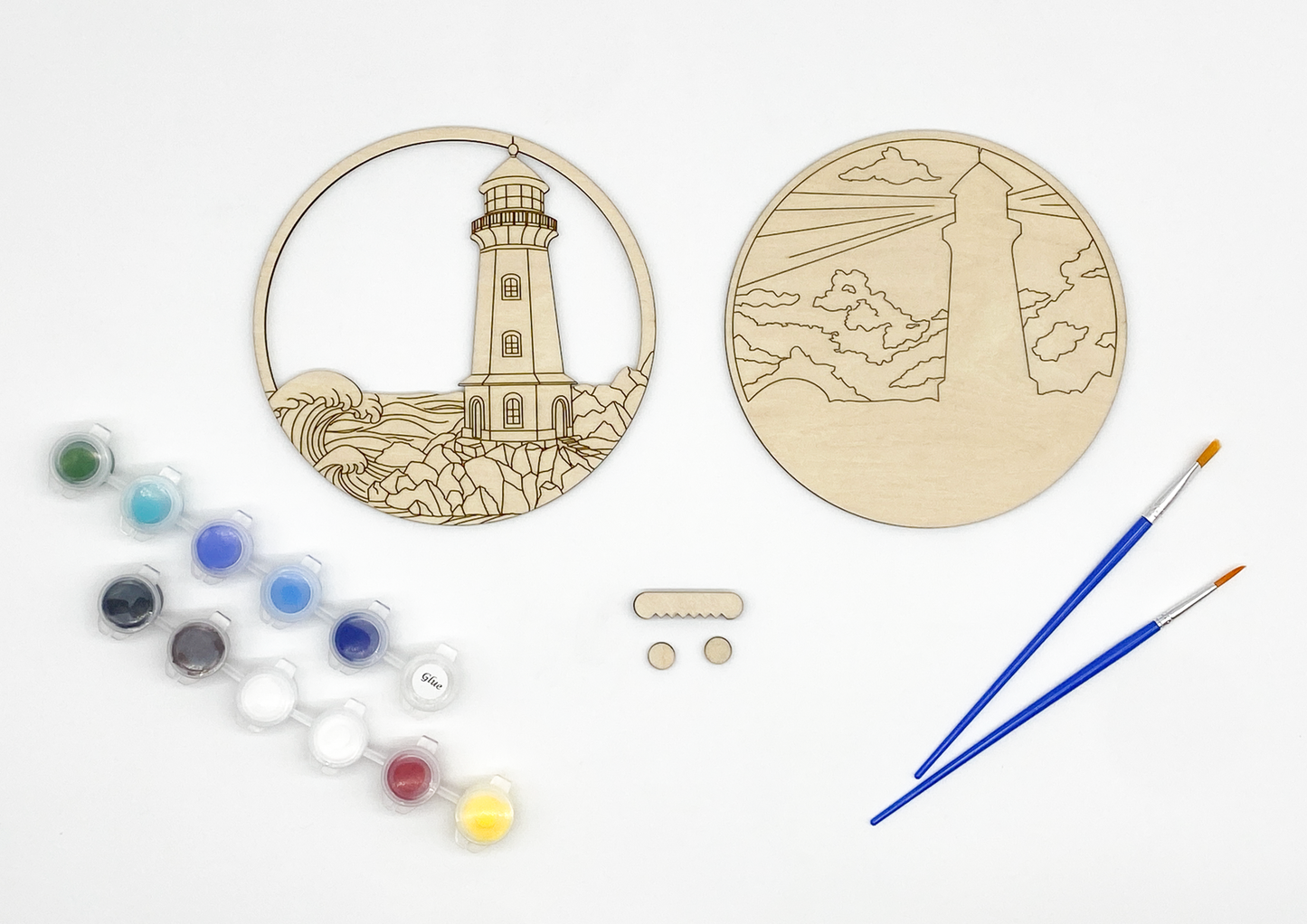 Lighthouse DIY paint kit contents showing two unpainted wood layers, paint pots, brushes, wall hanger, and bumpers
