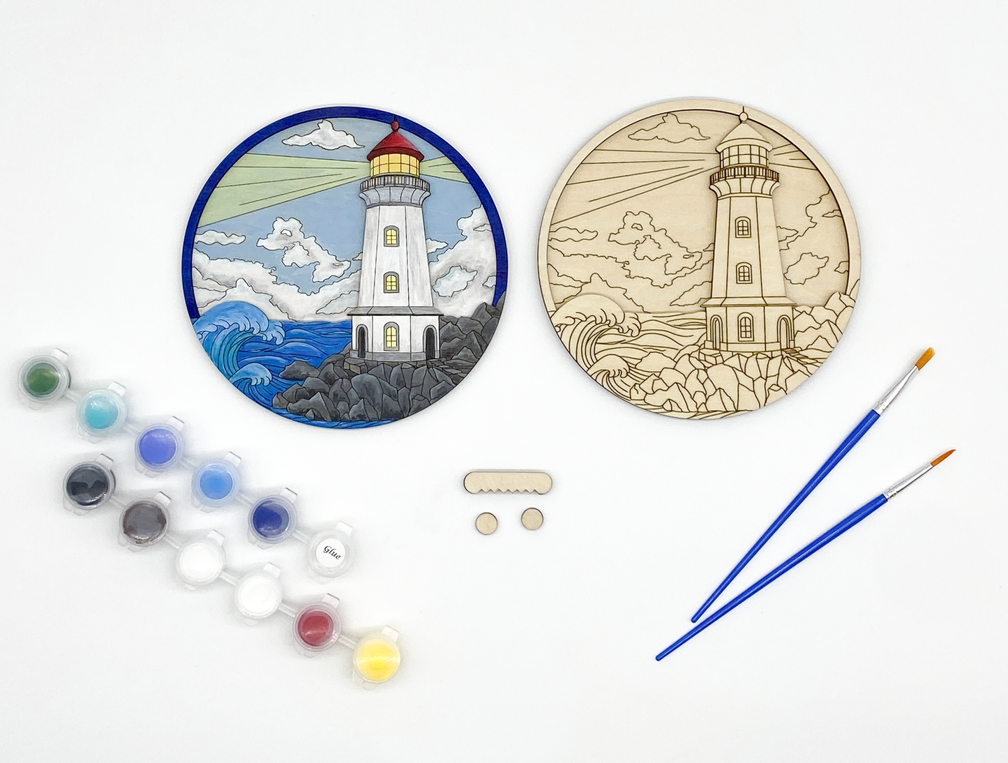Lighthouse craft kit with unpainted wood layers stacked together alongside paint pots, brushes, and hanging hardware