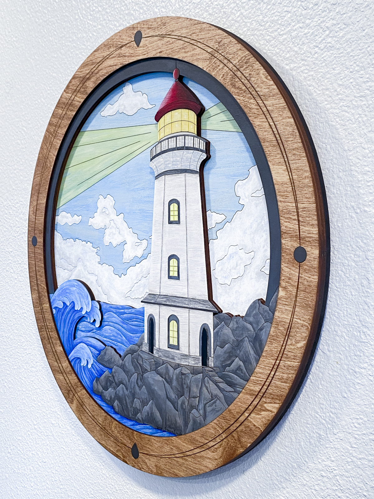 A full view of the finished "Lighthouse on a Rocky Shore" piece in a studio setting, showcasing the vibrant colors and custom-built circular frame.