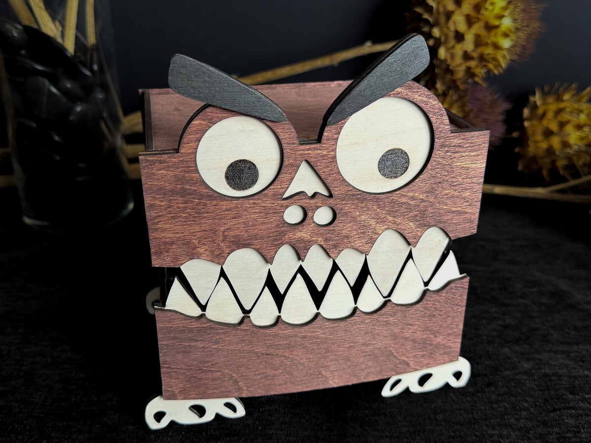 Mahogany-stained wooden monster keepsake box with oversized googly eyes, black eyebrows, layered white teeth, and small white feet.