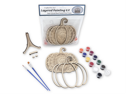 Complete Mandala Pumpkin adult painting kit with layered wood pieces, paint pots, brushes, glue, display stand, hardware, and packaged instruction card.