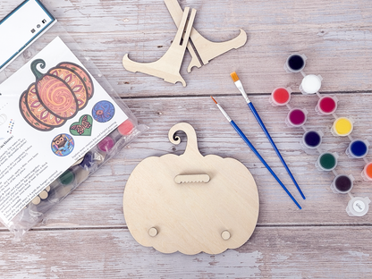 Back of the Mandala Pumpkin wood craft kit showing the hanger piece, small bumpers, display stand, paint pots, brushes, and packaging.
