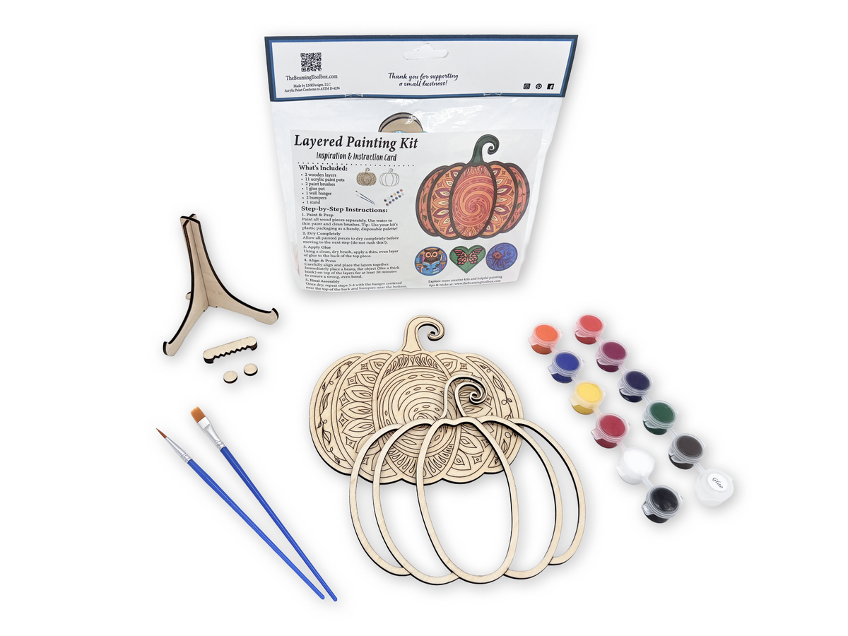 Mandala Pumpkin layered painting kit with unfinished wood pieces, paint pots, brushes, glue, display stand, hardware, and packaged guide.