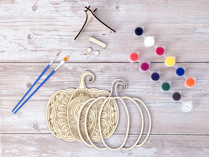 Unfinished Mandala Pumpkin wood craft kit pieces arranged with paint pots, brushes, display stand, hanger hardware, and bumpers.