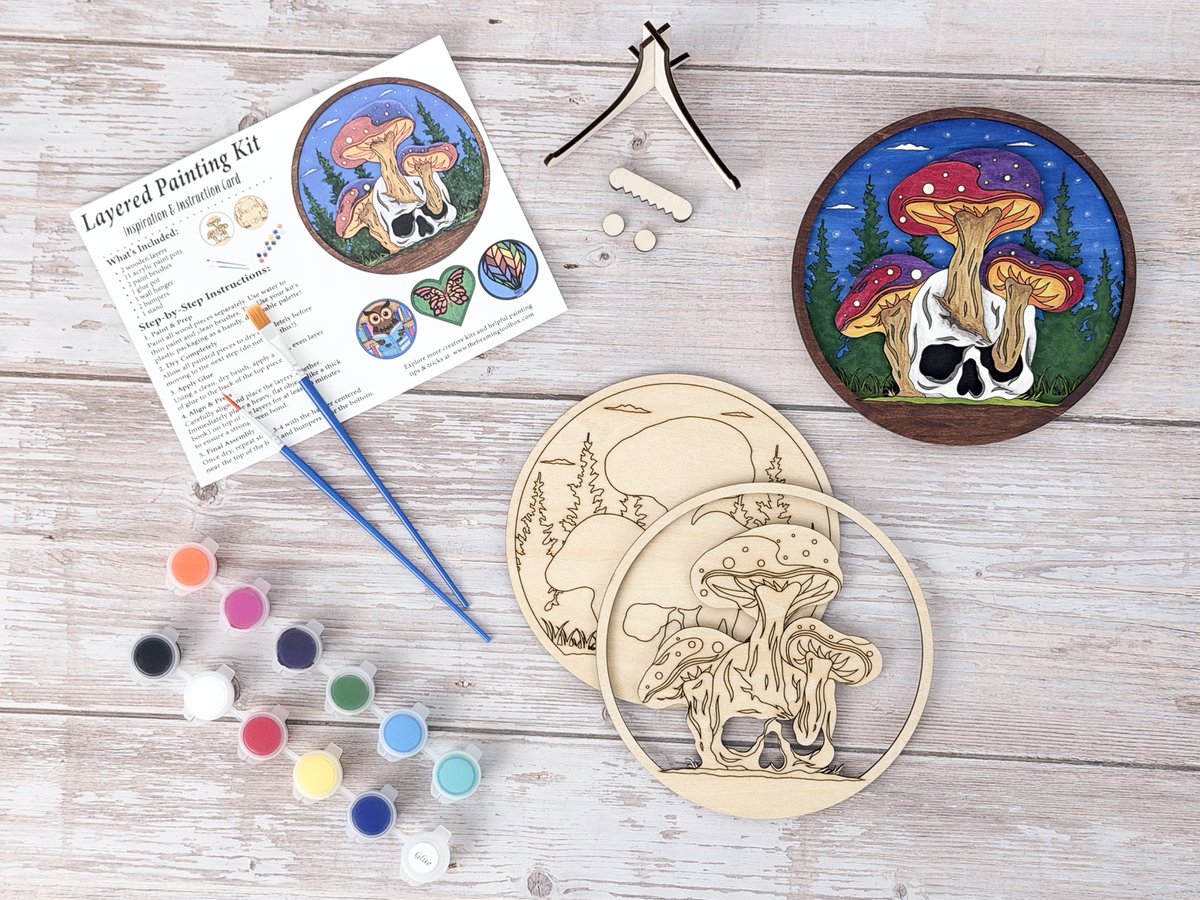 Mushroom Skull DIY wood painting kit with unfinished layers, paint pots, brushes, display stand, packaging, and a finished painted example.