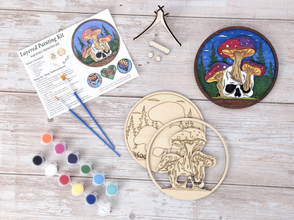Mushroom Skull DIY wood painting kit with unfinished layers, paint pots, brushes, display stand, packaging, and a finished painted example.