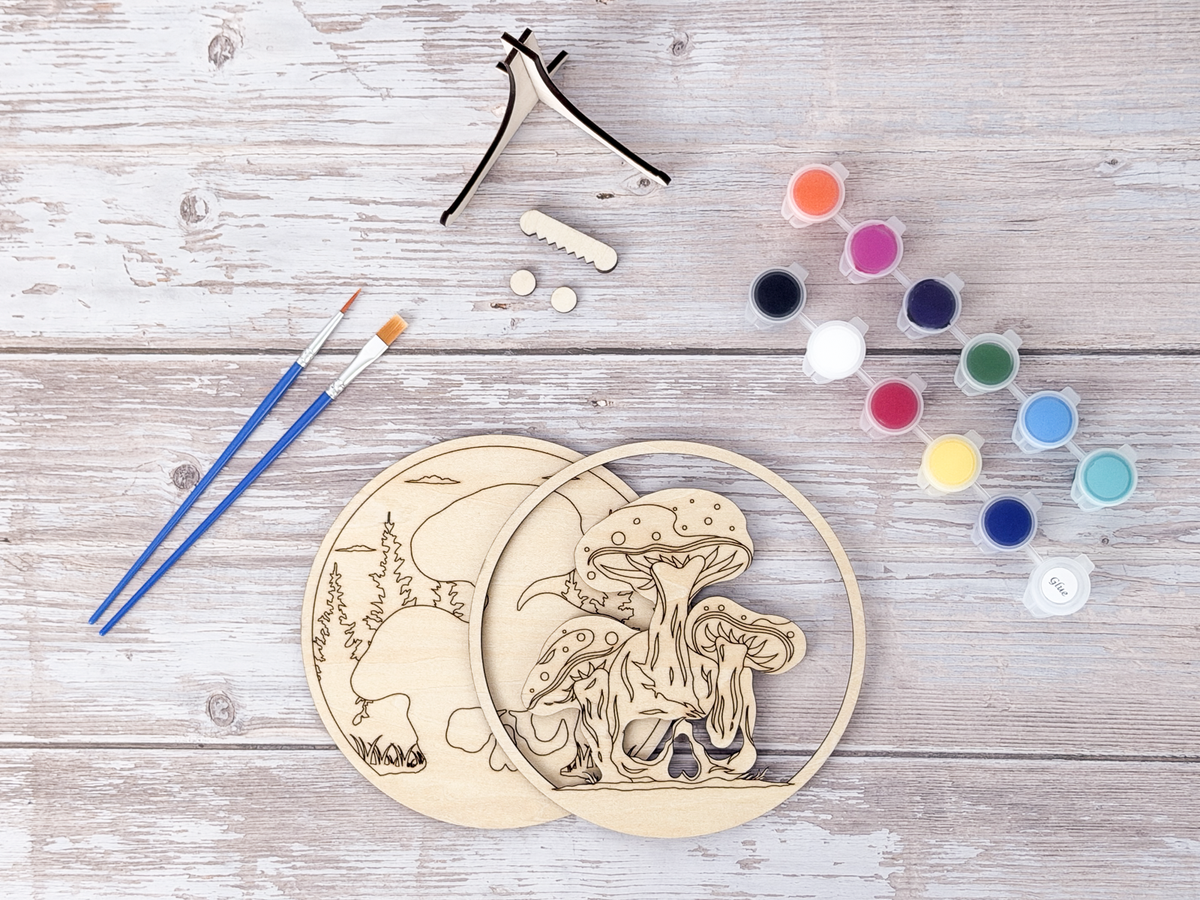 Unpainted Mushroom Skull wood craft kit displayed with paint pots, brushes, and stand pieces on a rustic wood background.