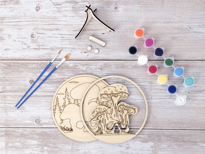 Unpainted Mushroom Skull wood craft kit displayed with paint pots, brushes, and stand pieces on a rustic wood background.