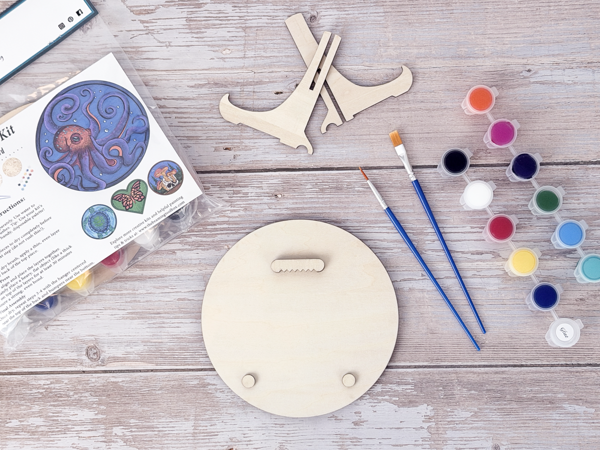 Back of the octopus wood craft kit showing the hanger piece, small bumpers, paint pots, brushes, stand pieces, and packaging.