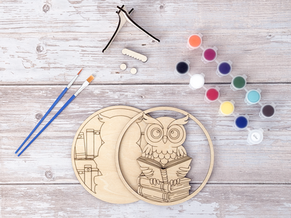 Unfinished book lovers owl wood craft kit pieces arranged with paint pots, brushes, display hardware, and packaging.