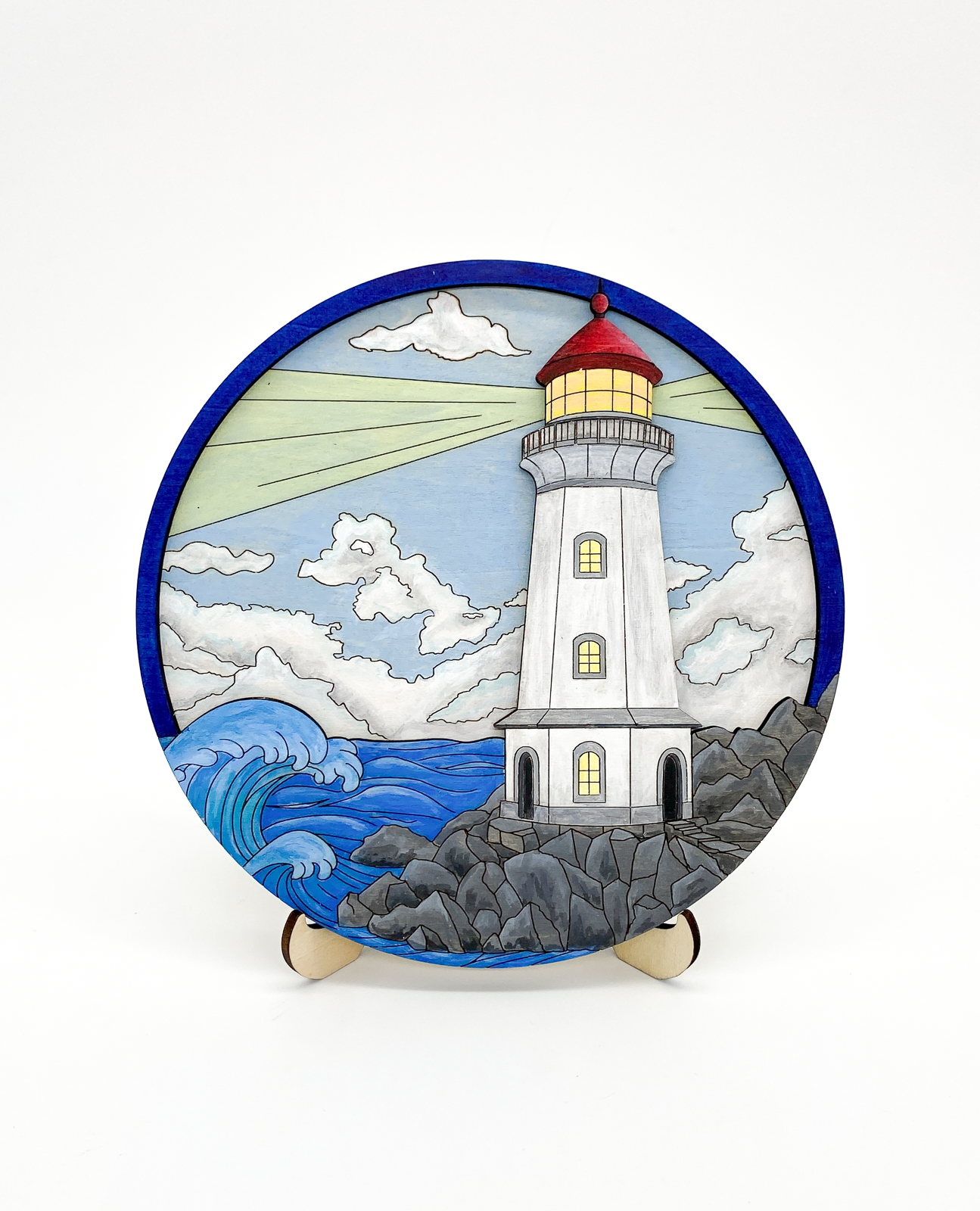 Front view of completed painted lighthouse layered wood art displayed on stand with ocean waves and light beam