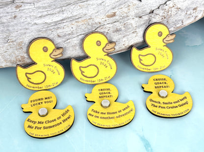 Yellow wooden cruise ducks displayed with custom ship names, sailing dates, engraved messages, and silver magnets against a coastal-inspired background.