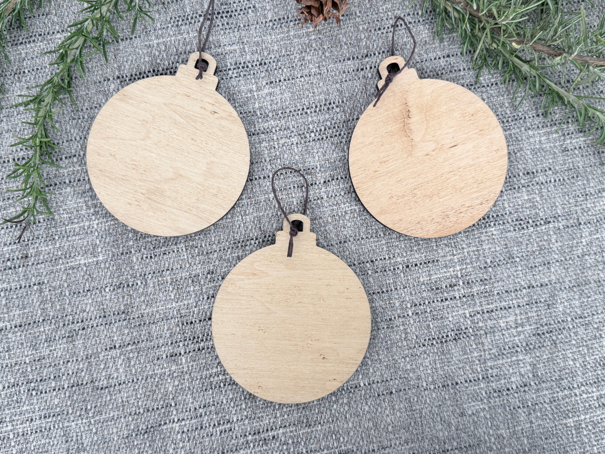 Back view of three wooden Sasquatch Christmas ornaments showing the natural wood surfaces available for custom message engraving.