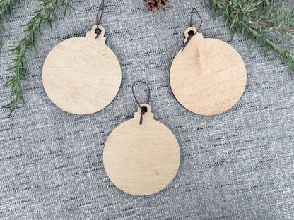 Back view of three wooden Sasquatch Christmas ornaments showing the natural wood surfaces available for custom message engraving.