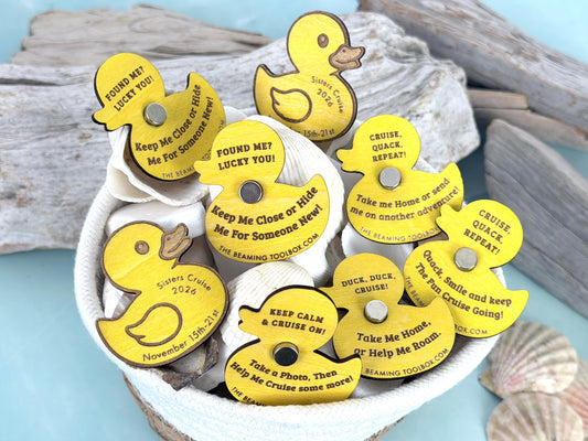 Personalized yellow wooden cruise duck magnets displayed in a white basket with seashells, featuring engraved cruise names, sailing dates, and playful messages.