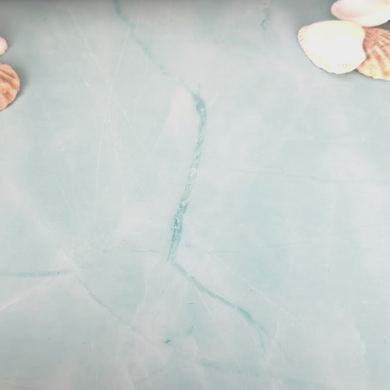 Two personalized wooden cruise ducks shown by hand, turning to display the engraved front and back before moving out of frame on a light blue background with shells and driftwood.