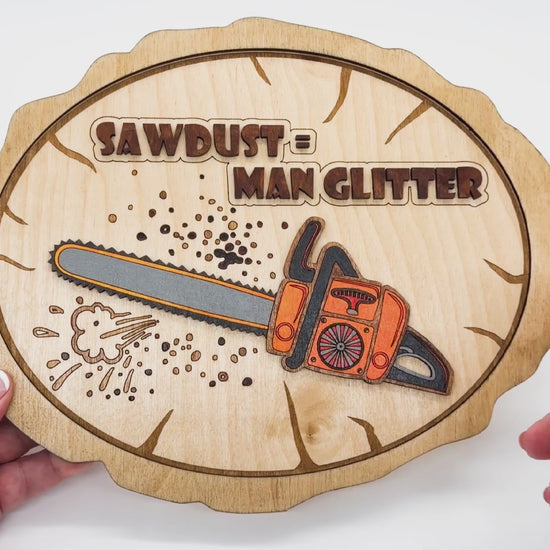 Video of Sawdust Equals Man Glitter showing the front and back with a colored chainsaw on front of a sign that is a faux wood round.