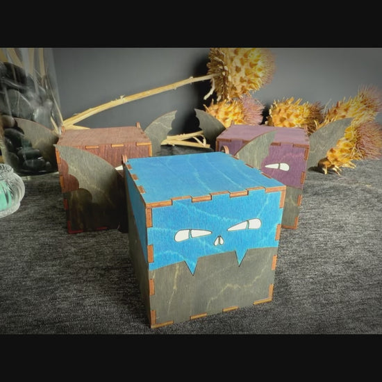 Video description: Handmade wooden bat keepsake boxes in blue, brown, and purple, featuring decorative bat wings, engraved faces, and hinged lids for storing small treasures.