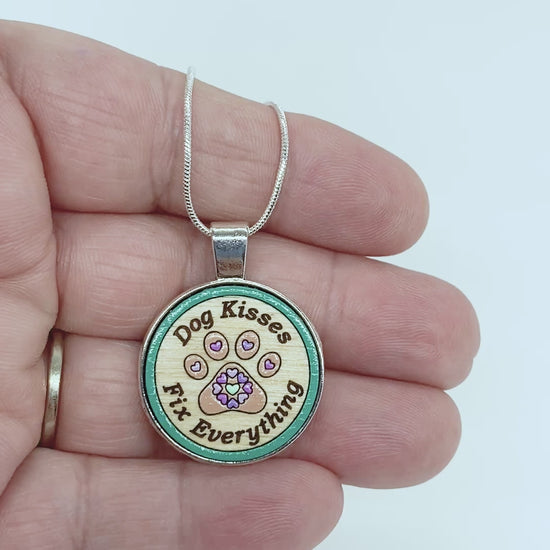 Video of handcrafted dog-themed necklace with engraved “Dog Kisses Fix Everything” text and paw print design in silver setting