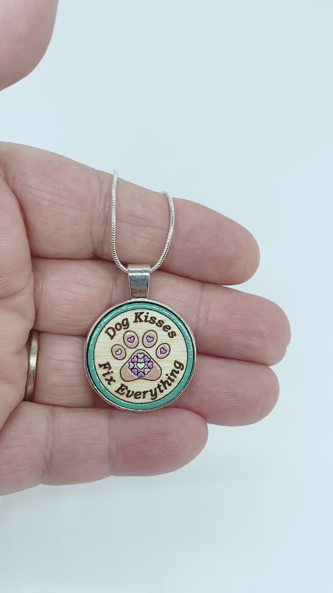 Video of handcrafted dog-themed necklace with engraved “Dog Kisses Fix Everything” text and paw print design in silver setting