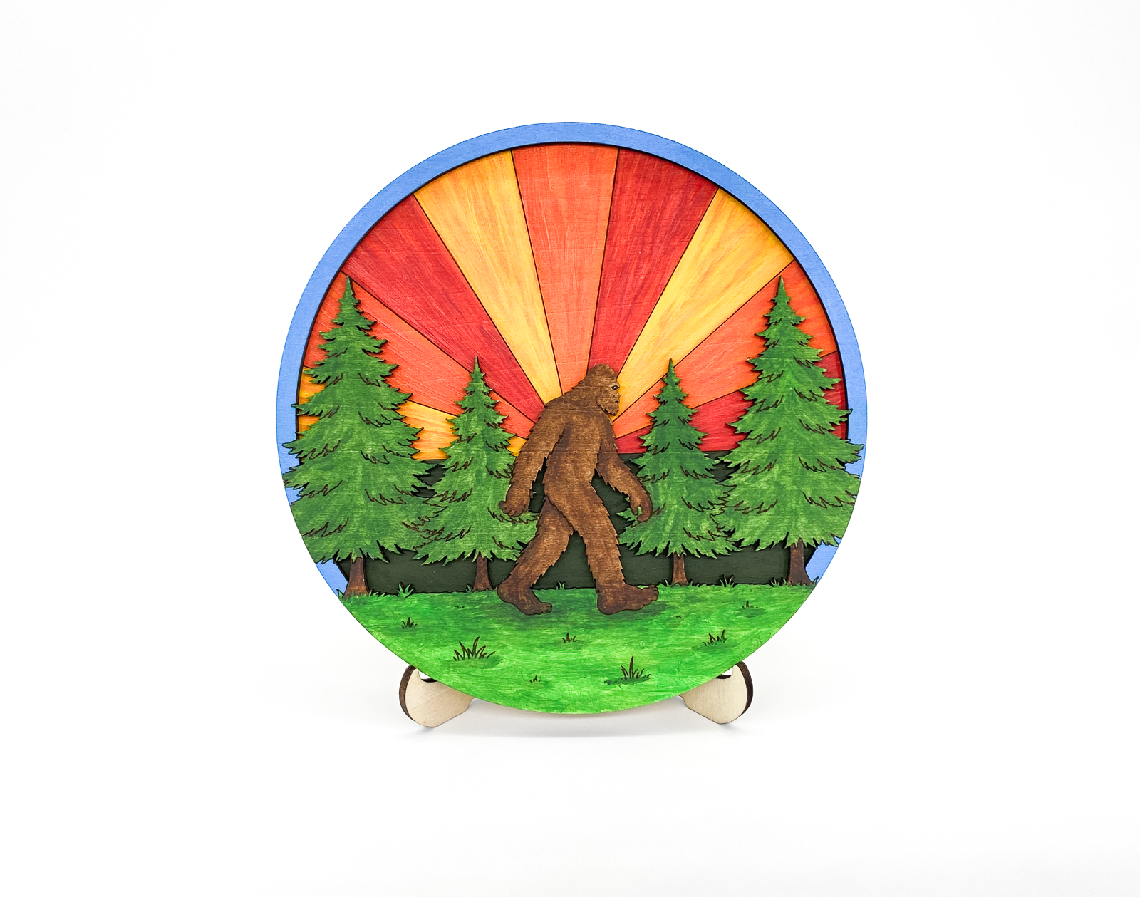 Finished 6-inch Sasquatch in the Forest DIY wood paint kit featuring a vibrant orange and red sunburst sunset and four evergreen trees