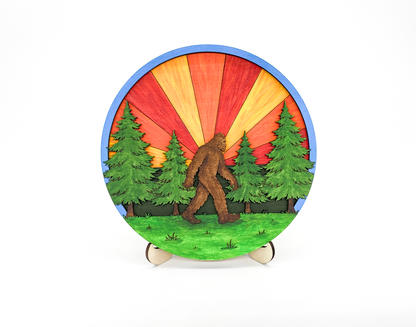 Finished 6-inch Sasquatch in the Forest DIY wood paint kit featuring a vibrant orange and red sunburst sunset and four evergreen trees