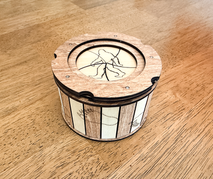 Handcrafted Sasquatch iris box made from basswood with natural wood and mahogany accents, featuring a twist-open lid, Bigfoot silhouette engraving, and footprint details around the sides.
